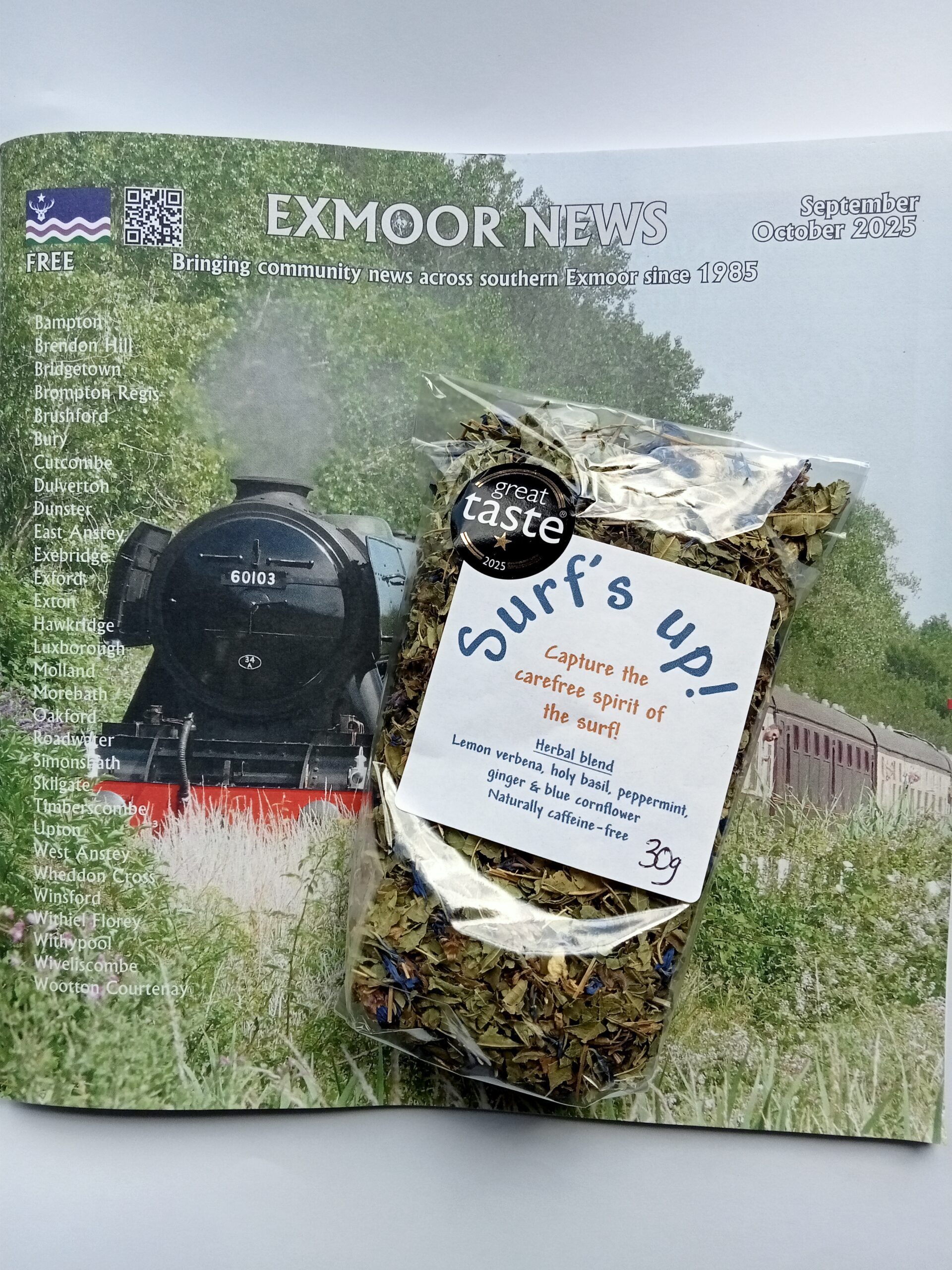 A bag of Surfs up! herbal tea rests on a copy of Exmoor News magazine, which features a steam train travelling through greenery on the cover. The magazine is for September/October 2025.